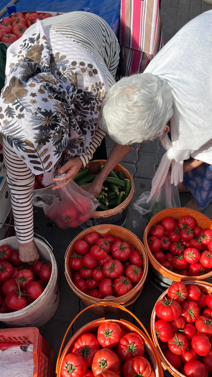 Personas eligiendo tomates y pepinos frescos en un mercado