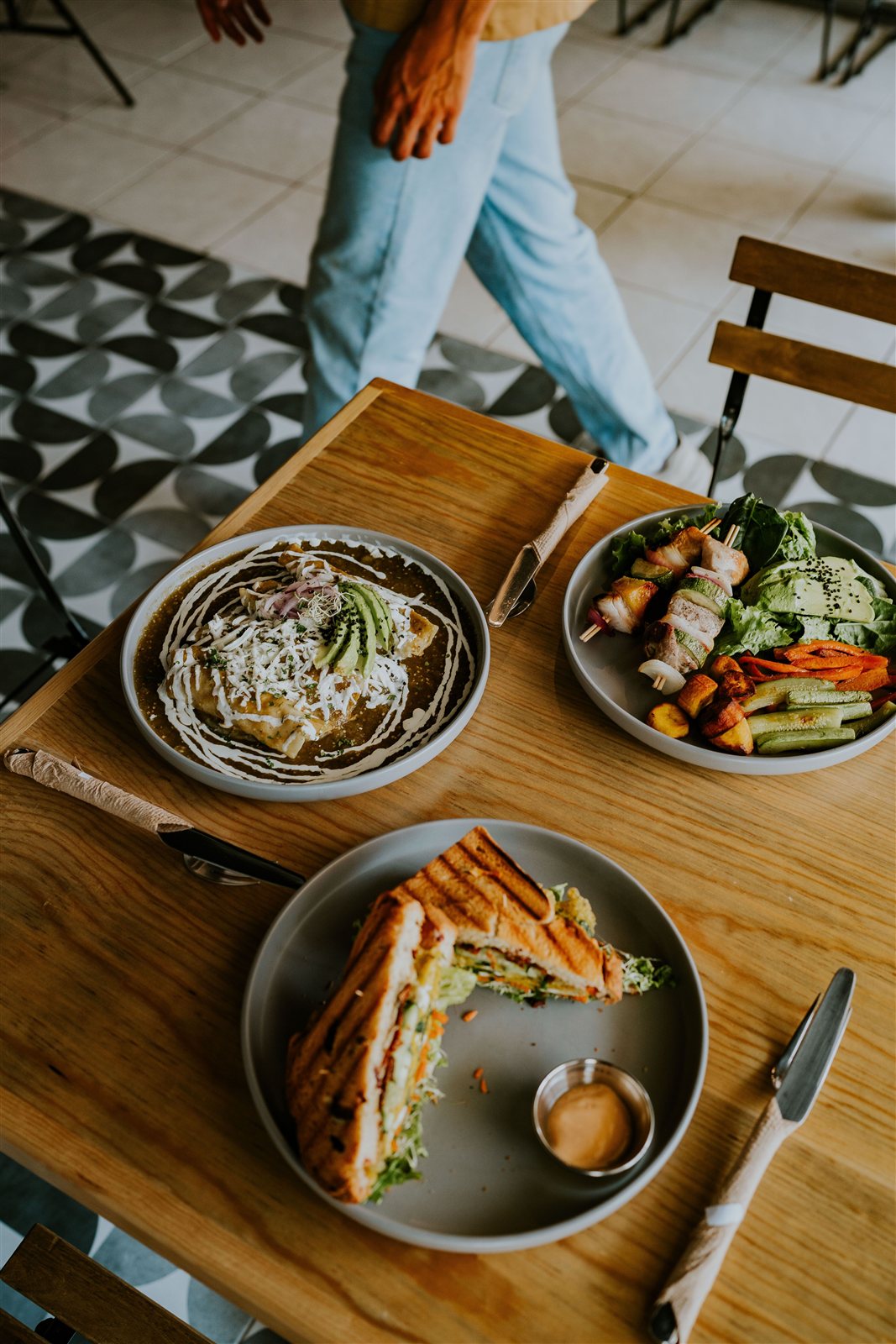 Mesa de restaurante con varios platos servidos y camarero de fondo